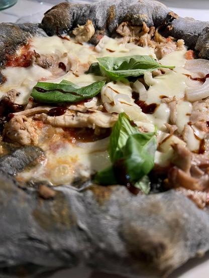 Charcoal dough pizza with tomato sauce, garlic, rabbit meat, mozzarella, onions and fresh basil.