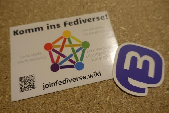 Ein Fediverse Flyer und ein Mastodon Flyer liegen nebeneinander auf einer Spanplatte.