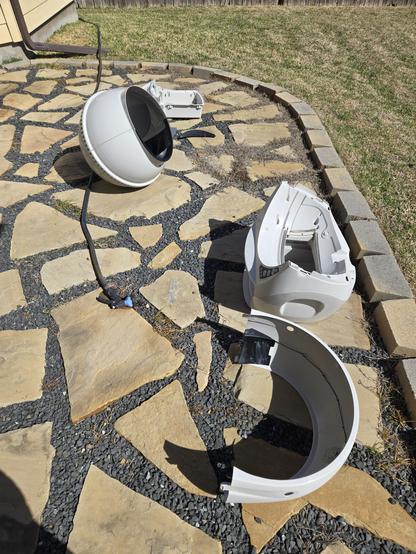 A picture of my disassembled Litter Robot on the backyard stone patio. A garden hose is laying next to it.  Grass is visible in the background.