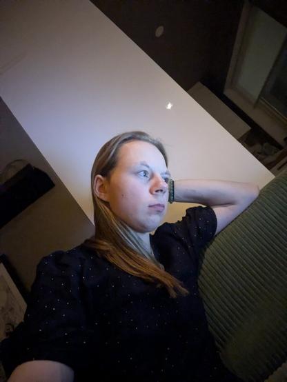 The image captures a woman relaxing on a couch. 

She is leaning back, seemingly deep in thought.

The setting is indoor, with a plain ceiling and a window in the background.

The foreground is dominated by the person and the green couch.