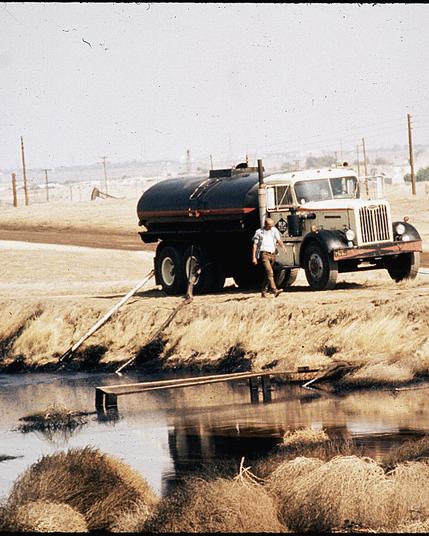 1970s photo of a man dumping oil into a pond in the Central Valley