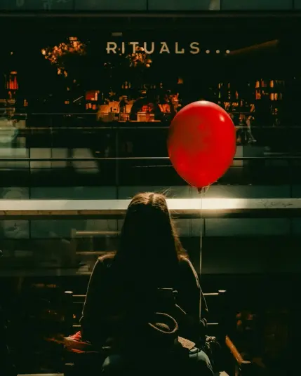 A woman backlit and in shadow next to a red balloon captured  in afternoon light.
