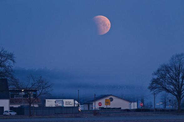 Der teilweise verfinsterte Mond über Bäumen und Häusern.
