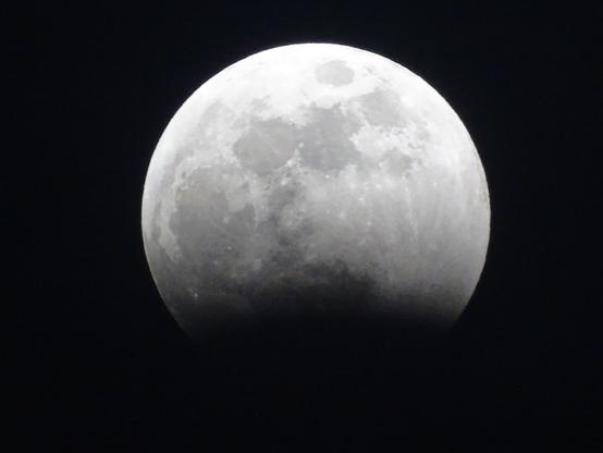 A full moon, the various features on the surface clearly visible against the pitch black sky. The bottom quarter is dark as the shadow of the earth begins to cover the bright sun lit side.