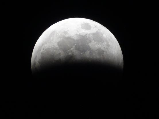 A full moon, the various features on the surface clearly visible against the pitch black sky. The bottom third is dark as the shadow of the earth begins to cover the bright sun lit side.