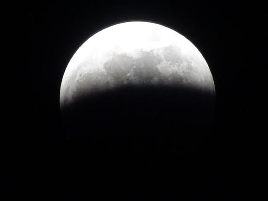 A full moon, the various features on the surface clearly visible against the pitch black sky. The bottom half is dark as the shadow of the earth begins to cover the bright sun lit side.