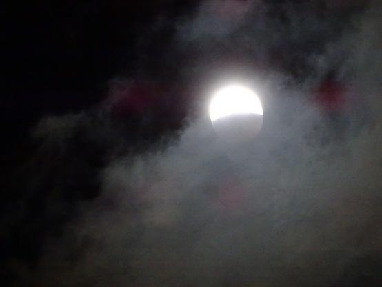 Wide view of the full moon, the remaining visible half shining brightly as the camera has zoomed out to catch the edge of the thick cloud that filled the sky and blocked any chance of seeing the rest of the eclipse.