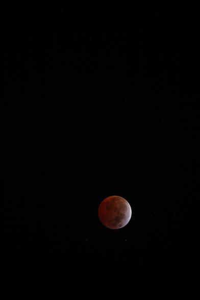 Luna llena con tono rojizo debido a eclipse total de luna, fondo completamente negro con algunas estrellas visibles