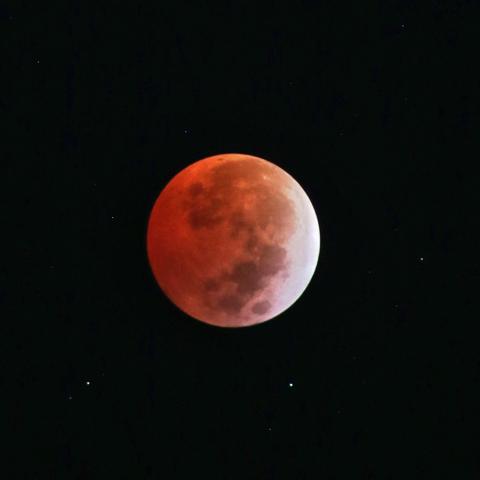 Luna llena con tono rojizo debido a eclipse total de luna, fondo completamente negro con algunas estrellas visibles