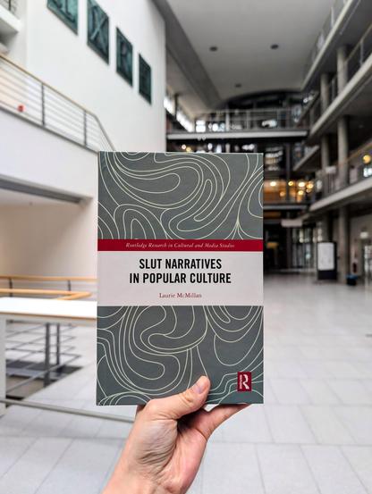 Holding the book "Slut Narratives in Popular Culture" by Laurie McMillan in the foyer of SUB library