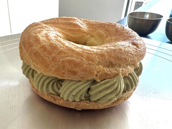 A choux pastry ring donut filled with pistachio whipped buttercream (crème mousseline) on the turntable, before being decorated