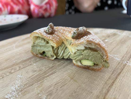 Cross-section cut of the ring donut showing the pistachio whipped buttercream filling and the candied pistachios on a bed of pistachio praline