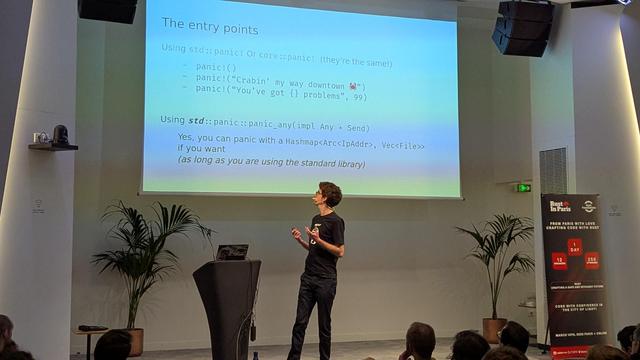 Arthur Carcano in front of a room. A slide on rust std/core panic is behind him on a big screen.