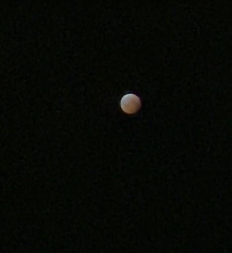 Slightly soft focus full moon during eclipse March 14 2025 in a dark sky showing slightly red from shadow cast upon it.