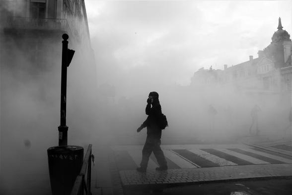 Un•e manifestant•e passe sur un passage piétons, seul•e au milieu d'un nuage de gaz lacrymogène