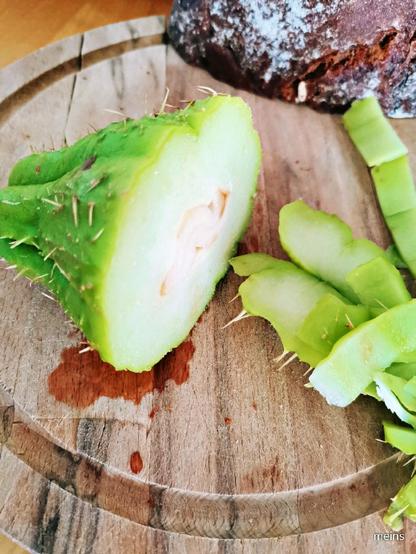 Auf einem runden Holzbrett liegt ein halbiertes Chayote-Kürbis mit hellgrüner Schale und Stacheln. Ein Teil der Schale ist bereits in Stücken abgeschnitten. Das Fruchtfleisch ist hellgrün bis weißlich. Unter dem Kürbis ist eine kleine Menge braune Flüssigkeit zu sehen. Im Hintergrund liegt ein Stück dunkles Brot.

Bereitgestellt von @altbot, generiert mit Gemini