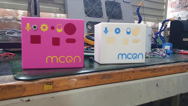 3d printed enclosure. Predominantly white but with a blue mcqn logo on the bottom right and a pink enclosure with a yellow mcqn logo