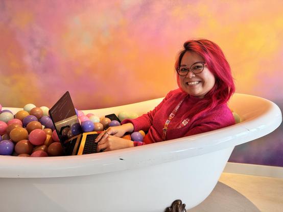 Me sitting in a bathtub of plastic balls with my laptop, taking notes.