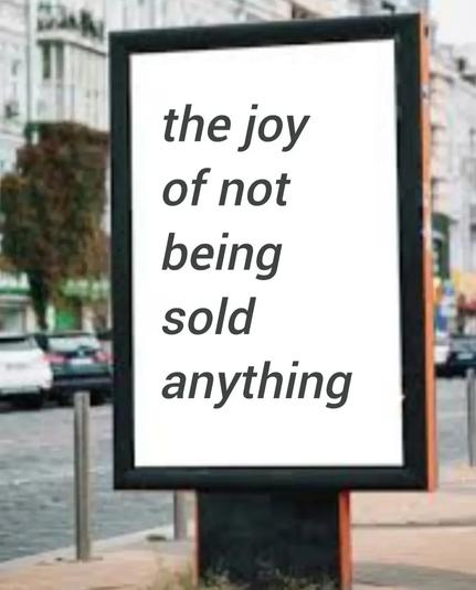 Poster on the street, trees and cars in the background, simple black letters on white background with a bold frame 

'The joy of not being sold anything'