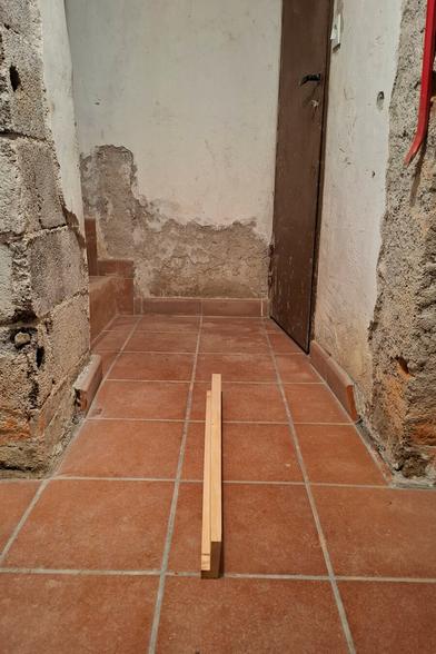 Custom made wooden beam made out of arolla pine lies on cellar floor which is tiled with terracotta.  The walls are made of a mix of exposed bricks, crumbling plaster, and rough concrete.