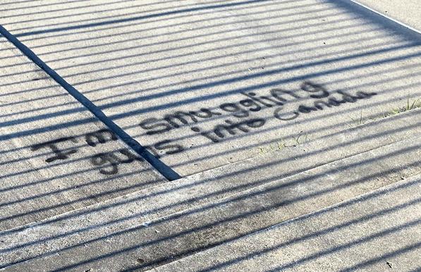 The phrase "I'm smuggling guns into Canada" spray painted on a concrete walkway, crossed with shadows from railing.