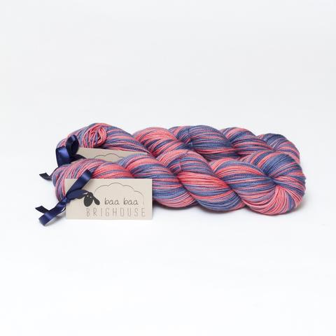 Picture shows two skeins of yarn, one behind the other, in shades of red and dark blue.