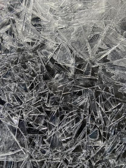 A pile of bright white triangular ice shards, with bright edges in the sun. In some parts we can see the black of the underlying asphalt