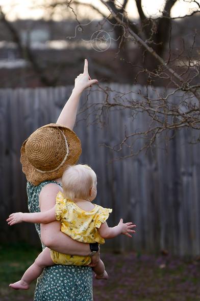 A mother points out a bird in a tree to the child in her arms.
