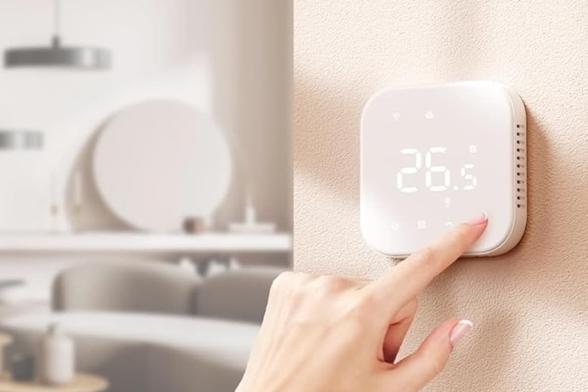 Eine Hand bedient das an einer Wand angebrachte Thermostat von Meross, auf dem eine Temperatur von 26,5 Grad angezeigt wird. Foto (c) Meross.