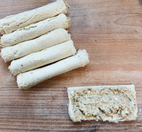 ein Stück Toastbrot mit der Ziegenkäsecreme bestrichen, daneben 5 bereits fertig gerollte Scheiben