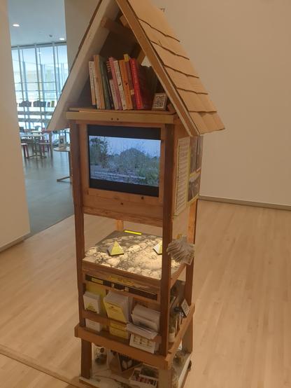 The same structure from the other side. There are more books below the roof, and a TV monitor showing a video about seed collecting where the drawers would be. There are pamphlets on the lower platform.