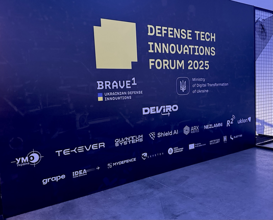 Eine Wand auf der die Sponsoren des Defense Tech Innovations Forum 2025 aufgelistet sind. Die Wand ist dunkel gehalten.