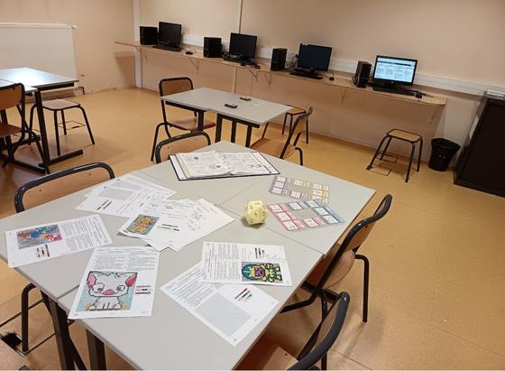 Photographie d'une table avec des pixel art dessus un dé à 20 faces un classeur ouvert et des cartes de révision ranger dans des pochettes dédiées.
