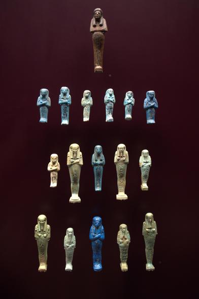 Nom : Ouchebtis
Auteur : Culture égyptienne de Deir-Al-Bahari (XIXe dynastie)
Date : -1295 — -1186
Type : Sculpture sur bois
Source : Musée des Confluences (Lyon, France)
Cote/Inv. : 90002924
Document : ORAEDES (2023)
Commentaire : Élément important du mobilier funéraire égyptien, les ouchebtis sont des serviteurs post-mortem exécutant les corvées au Champs d'Ialou pour le défunt dans l'au-delà. Ces corvées sont en effet nécessaire au maintient de l'intégrité de son ka, sous réserve que les vivants ne s'en occupent pas par le truchement d'offrandes. Censées représenter le mort, on trouve sur chacun des ouchebti, le nom de sa fonction et son propriétaire. Une série complète est censée contenir assez d'ouchebtis pour chaque jour de l'année raison pour laquelle on dispose d'un grand nombre de ces statuettes dans les musées d'antiquités.