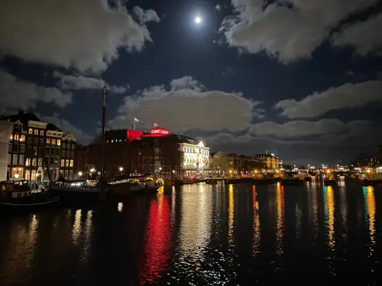 Theater Carré at the river Amstel in Amsterdam. Lights reflecting in water. Moon visible.
