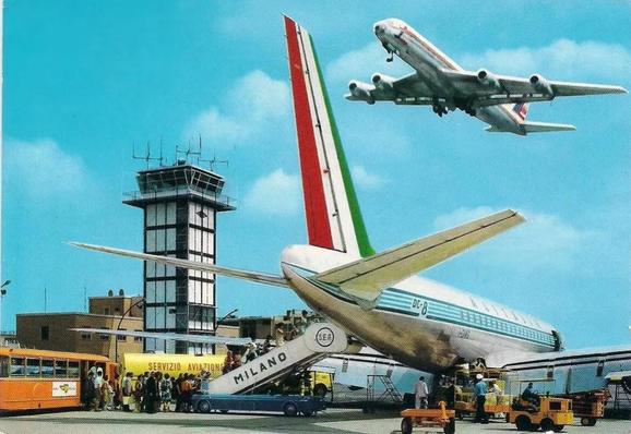The view is of passengers boarding the Alitalia jet in front of the tower. There is a second jet flying overhead