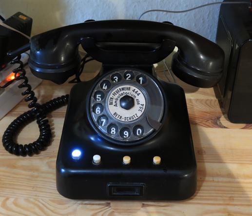 A rotary dial telephone "Vorzimmerapparat 38" by "VEB Fernmeldetechnik Nordhausen" with a lit light.