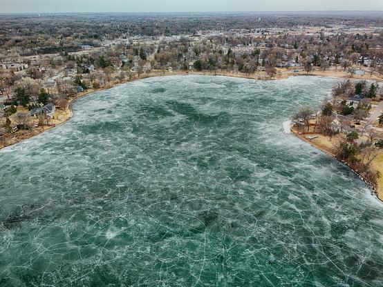 View of a lake from above with cracks forming in the ice