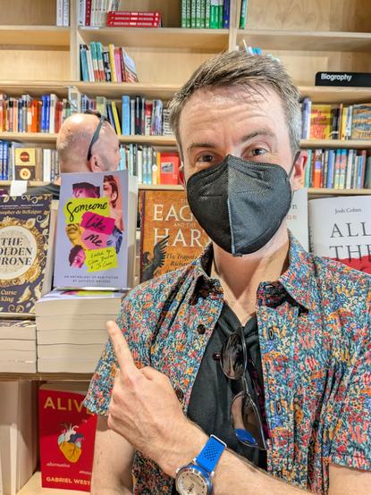 I'm standing in a bookstore wearing a black face mask and pointing at a copy of the anthology Someone Like Me, a anthology of autistic women and gender diverse writers.
