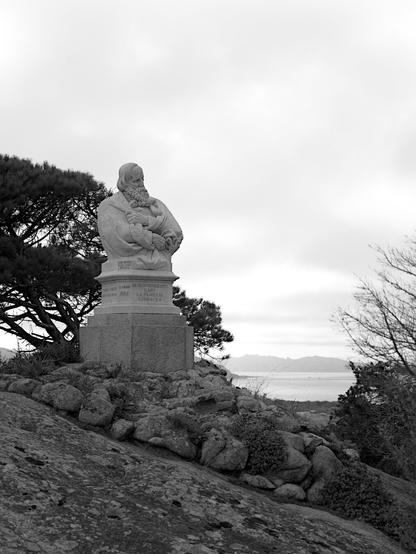 A black and white picture of a monument to Garibaldi, on rocky terrain and overlooking the sea.