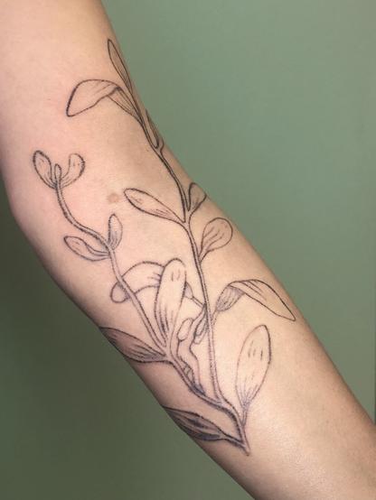 Tatouage d’une branche de sauge avec un petit personnage sur le bras