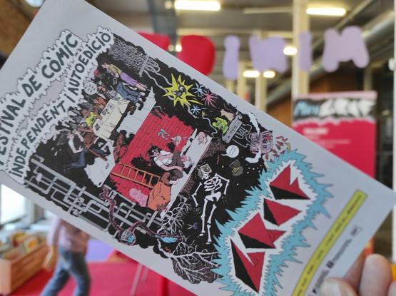 El folleto con la información básica del festival Graf en primer plano y de fondo el hall principal de la Fabra i Coats donde se celebra el festival de comic independiente y autoedición este fin de semana.