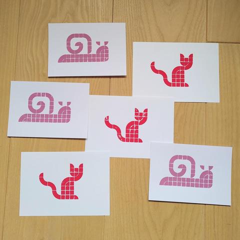 Postcard sized prints with either a silhouette of a cat or of a snail spread on a wooden floor.