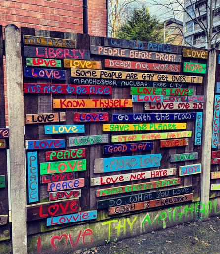 Fence in Manchester UK with lots of positive messages posted on it in various colours, reds, greens yellows, blues. "Love not Hate", "Peace",  "Love", "Save the Planet", "Joy", L❤️ve", "It's nice to be nice".
