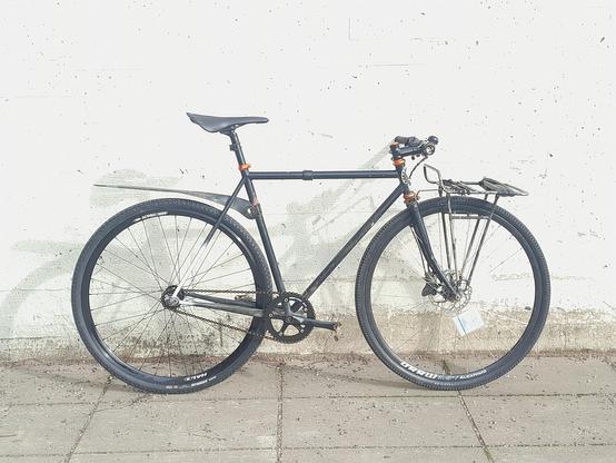 Black Surly Steamroller fixed gear bike with front rack and disc brake in front. Photographed from drive side.