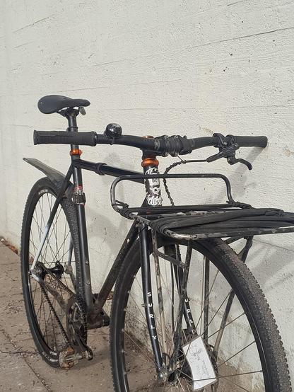 Black Surly Steamroller with front rack, photographed from front/drive side. Flat bar with hydraulic front disc brake. bc Hellsinki sticker on head tube, worn out frame.