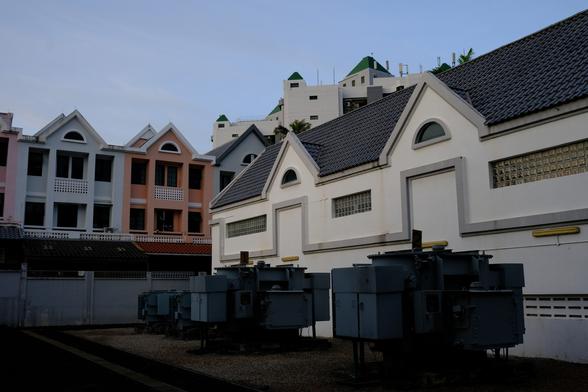 View of three power transformers in a courtyard with strongly geometric buildings behind.