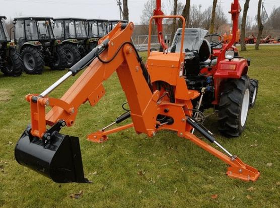 Example of a tractor attached digger. There's a red mini tractor at one end, with an orange excavator attached to the three point hitch. Not visible, but a hydraulic pump is clamped directly to the PTO shaft, powering the excavator from the tractor engine. A second backwards facing seat is mounted behind a guard rail with the excavator controls. Two hydraulic feet are lowered to fix the digger to the ground.