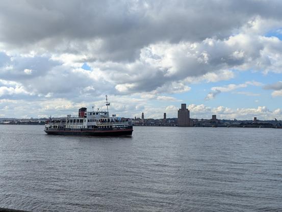 a passenger ferry boat on the River Mersey with buildings visible on the south bank in the distance