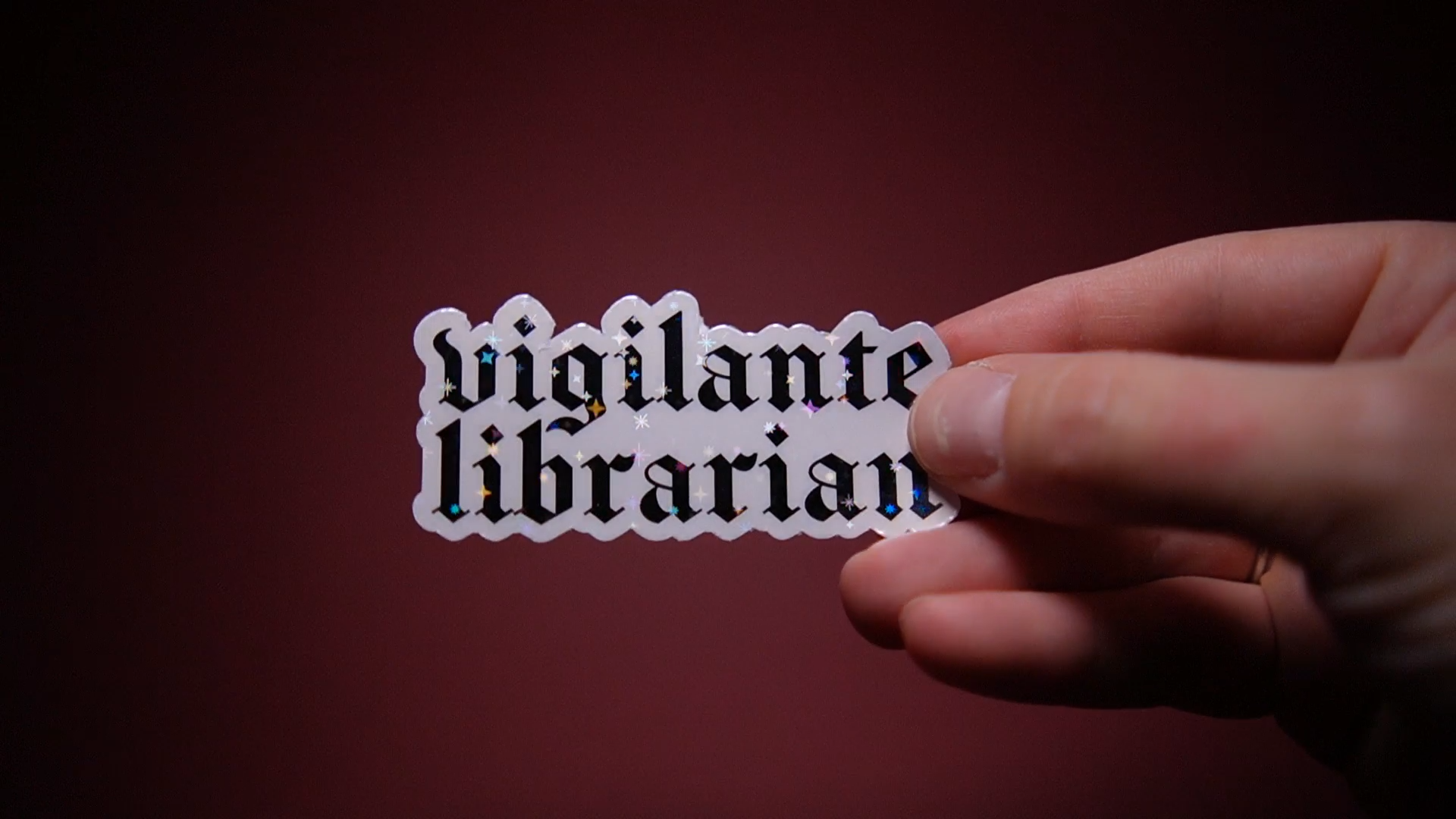 A sparkly vinyl sticker reading “vigilante librarian” in blackletter font